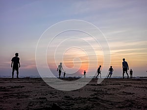 Boys playing football on the beach, beautiful sunset in background