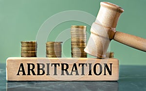 ARBITRATION - word on a white sheet with a judge's gavel and a stack of coins in the background