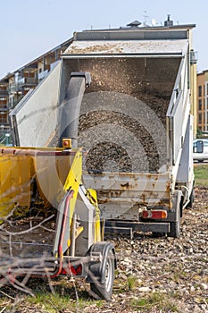 Arborist tipper with high sides together with a yellow branch chipper. The chipper`s mouth is visible with retraction rollers and