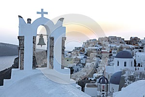 Arch with a bell, white houses and church with blue domes in Oia or Ia at golden sunset, island Santorini, Greece. - Immagine photo