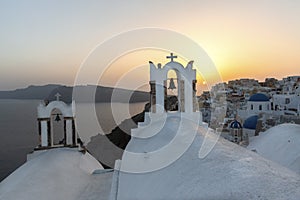 Arch with a bell, white houses and church with blue domes in Oia or Ia at golden sunset, island Santorini, Greece. - Immagine photo