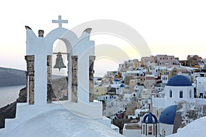 Arch with a bell, white houses and church with blue domes in Oia or Ia at golden sunset, island Santorini, Greece. - Immagine photo