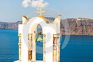 Arch with a bell, white houses and church with blue domes in Oia village. Island Santorini, Greece