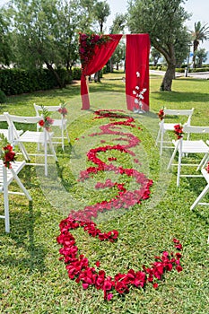 Arch and chairs decorated with fresh flowers in red tones for the wedding ceremony on the green lawn