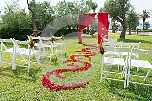 Arch and chairs decorated with fresh flowers in red tones for the wedding ceremony on the green lawn