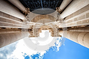 Arch and columns with capitals. Blue sky and clouds