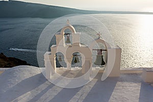 Arch with cross and bells of traditional Greek white church in Oia village, Santorini Island, Greece