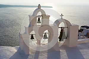 Arch with cross and bells of traditional Greek white church in Oia village, Santorini Island, Greece