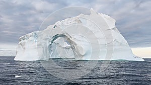 Arch in a huge iceberg, high breakaway glacier drifts in the southern ocean off the coast of Antarctica at sunset, the