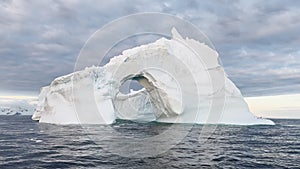 Arch in a huge iceberg, high breakaway glacier drifts in the southern ocean off the coast of Antarctica at sunset, the