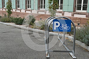 Arch metal frame for parking bicycles with blue sign containing letter P and pictogram of bicykle situated on the street.