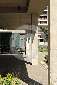 An arch passage below the modern building. Rectangular columns hold the construction. Bicycle parking area