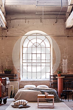 Arch window in a wabi sabi bedroom interior with a bed, raw walls and table photo