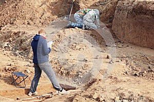 Archaeological excavations. The archaeologists in a digger process, researching the tomb with human bones, drawing the human remai