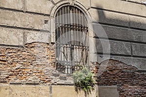 An arched barred window on the wall of an old house.