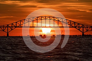 Arched bridge silhouette in front of large setting sun