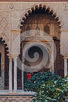 Arched entrance to Patio de Maidens courtyard inside Alcazar of Seville, Spain, tourist walk on background