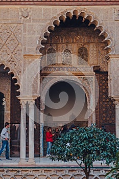 Arched entrance to Patio de Maidens courtyard inside Alcazar of Seville, Spain, tourist walk on background