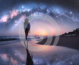 Arched Milky Way and young woman in hat on sandy beach