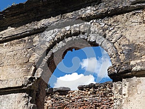 Arched opening of a ruined ancient red brick building against a blue sky