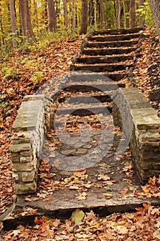 An arched stone bridge leading to stone steps up a hill in a forest preserve in the fall in Wisconsin