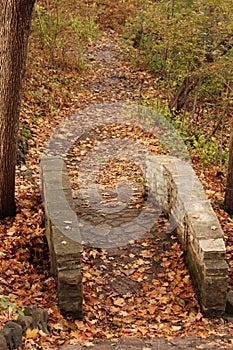 An arched stone bridge on a trail through the forest covered with fallen leaves during autumn in Kenosha, Wisconsin