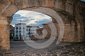 Arched stone gateway and old buildings at dusk in Caceres