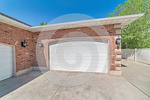 Arched white wooden garage doors against red brick wall and blue sky background