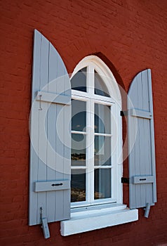 Arched window with open shutters on a red brick wall of the house