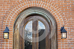 Arched window on a red brick building wall with lantern lamps on the side