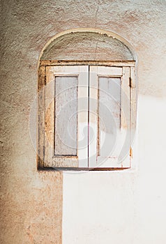 Arched window with two window shutters in a pale almost dirt coloured wall.