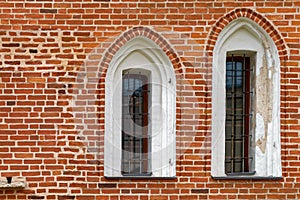 Arched windows with iron grill on an ancient red brick wall.