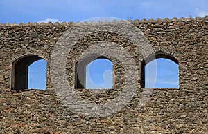 Arched windows in ruin stone wall against a blue sky, Italy