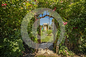 Arched wooden arbor at the entrance of a garden with playhouse slides and swings