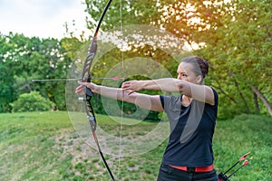 Archery in nature, young woman aiming an arrow at a target