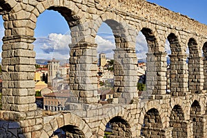 Arch detail of the Aqueduct of Segovia, with the tower bell of the Saint Justo y Pastor church in the background. View from photo