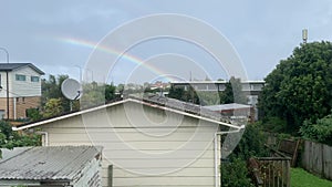 Arching rainbow formation over residential rooftops