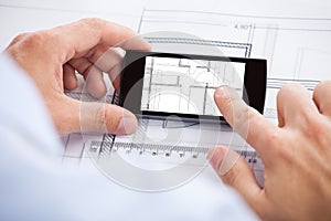 Architect Analyzing Blueprint On Mobilephone