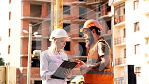 Architect and builder at construction site. Woman engineer and brutal builder communicate construction site background