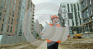 Architect or builder man walking on the construction site and analyzing scheme project plan. Young architect or builder