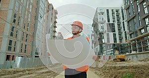Architect or builder man walking on the construction site and analyzing scheme project plan. Young architect or builder