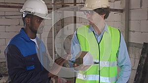 Architect and builder talking and holding model house at construction site.