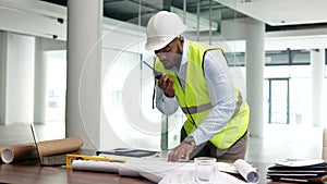 Architect, building engineer or construction worker looking at plans and blueprints and talking on a radio. Male