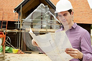 Architect On Building Site Looking At House Plans