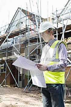 Architect On Building Site Looking At House Plans