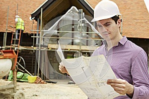 Architect On Building Site Looking At House Plans