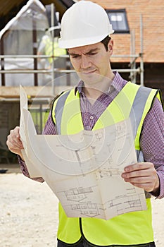 Architect On Building Site Looking At Plans For House
