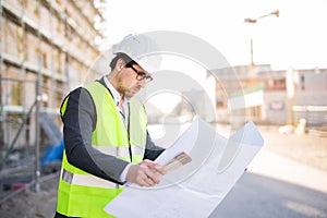 An architect / civil engineer at work on a construction site, holding plans in hand