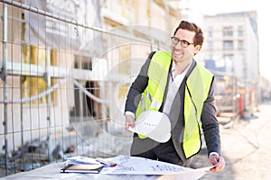 An architect / civil engineer at work on a construction site, holding plans in hand