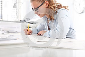 Architect drawing blueprints, at desk in office, with pencil